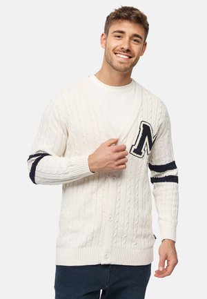 Cárdigan blanco de punto trenzado con escote en V, con botones en el frente, un parche de la letra "N" en color marino y acentos a rayas en azul marino en las mangas.