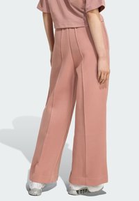 Hlače širokih nogavica od mekog ružičastog materijala s bočnim nabora, s glatkom teksturom i čistim rubom. Nosene s bijelim tenisicama.