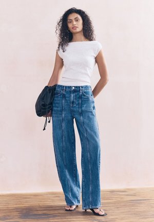 Fehér, testhezálló felső virágos hímzéssel. Magas derekú, bőszárú kék farmer. Fekete húzózsinóros táska és pántos szandálok teszik teljessé a megjelenést.