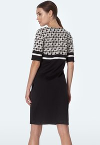 Czarna sukienka z materiału w wzór houndstooth w górnej części oraz jednolitej czerni w dolnej części, z krótkimi rękawami i okrągłym dekoltem.