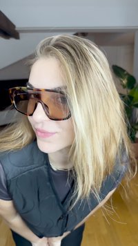 Üks suurte raamite vaheliste tortoosekiliste päikeseprillidega, millel on pruunid läätsed, nurgeline disain ja paksud raamid. Taust on heledates värvitoonides ja siseruum.