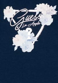 Navy sininen puuvillapaita, jossa on kukkakuva pehmeissä pastellisävyissä, tekstillä "Guess Los Angeles" ja kolmion muotoisella yksityiskohdalla.