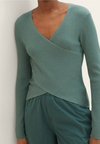 Morski niebieski prążkowany top na długi rękaw z dekoltem w serek i zakładanym fasonem, zestawiony z dopasowanymi, luźnymi spodniami w tym samym odcieniu. Gładka faktura i dopasowany krój.