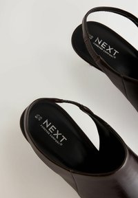 Ruskea nahkainen slingback-kengät pyöreällä varvaskohdalla, pehmustettu pohja ja elastinen hihna. "NEXT Forever Comfort" -brändäys näkyvissä sisäpuolella.
