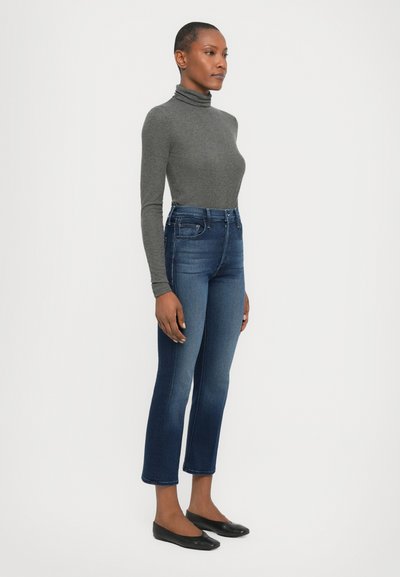 Jeans albastre cu talie înaltă, cu o siluetă ajustată, ușor decolorate și tiv evazat, asortați cu un pulover gri cu guler și pantofi negri cu talpă joasă.