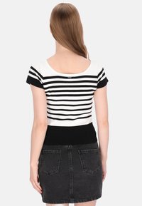 Zwart-wit gestreepte gebreide top met een scoop-back, korte mouwen en een aansluitende zwarte geribbelde tailleband; gedragen met een zwarte denim minirok.