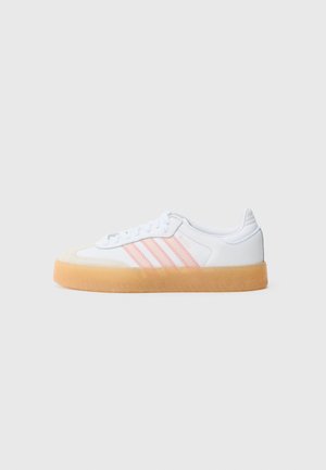 Biały niski sneaker z gumową podeszwą i trzema jasnoróżowymi paskami po boku, pokazany z profilu prawej strony na szarym tle.