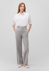 Pantaloni a righe grigie a gamba larga con vestibilità sartoriale, dotati di tasche anteriori e chiusura con bottone, abbinati a una camicia bianca con bottoni.