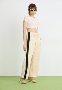 T-shirt court crème à manches courtes, pantalon large beige avec des rayures noires sur les côtés, et baskets beiges avec un logo discret.
