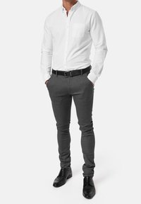 Chemise blanche boutonnée avec une poche poitrine, associée à un pantalon gris ajusté et des chaussures en cuir noires, avec une ceinture noire.