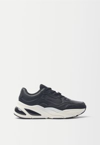 Sneaker in pelle nera con dettagli testurizzati, chiusura con lacci sul davanti, suola intermedia bianca spessa e suola esterna in gomma nera; design snellito con forma unica.