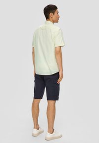 Lichtgele shirt met korte mouwen, marineblauwe cargoshorts en witte sneakers. Het shirt heeft een rechte zoom en een knoopsluiting bij de kraag, met een gestructureerde stof.