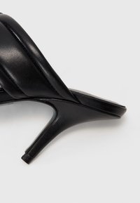 Svart klacksandaler med ett slätt läderövertyg, öppen tå-design och en smal, avsmalnande klack, som visar en minimalistisk silhuett.