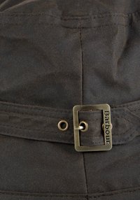 Κοντινό πλάνο ενός σκοτεινού υφασμάτινου ζώνης με μεταλλική αγκράφα χαραγμένη με τη λέξη Barbour, στερεωμένη μέσω μεταλλικού κρικάκι.