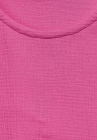 Primo piano di un tessuto rosa strutturato con una cucitura curva, che mostra dettagli intrecciati fini e sottili variazioni di colore.