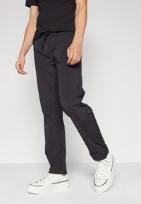 Sorte tapered bukser med elastisk talje og snøre, der har en glat tekstur og sidelommer, parret med hvide sneakers.