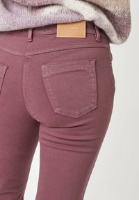 Mauve Jeans mit einer figurschmeichelnden Passform, ausgestattet mit zwei Gesäßtaschen und einem strukturierten, hellbraunen Lederetikett am Bund. Glatte Stofftextur.