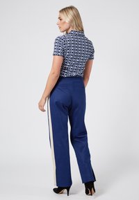 Blå mönstrad skjorta med kort ärm och krage, kombinerad med marinblå byxor med en kontrasterande beige sidostripe och slitsar i fållen.