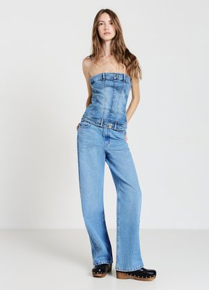 Blaues Denim-Trägershirt ohne Träger mit Nahtdetails und Knopfakzenten, kombiniert mit weit geschnittenen blauen Jeans und schwarzen Holzclogs mit Nieten.