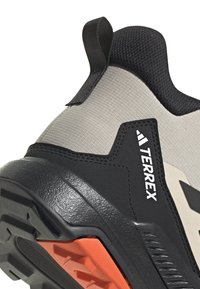 Chaussure de sport grise et noire avec un upper texturé, semelle en caoutchouc durable, accent orange et logo TERREX bien visible sur le côté.