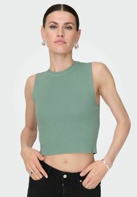 Jasnozielony, prążkowany crop top z okrągłym dekoltem i bezrękawnikowym fasonem, połączony z czarnymi spodniami o wysokim stanie, o delikatnej fakturze.