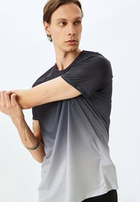 Camiseta atlética de manga corta en degradado de negro a gris, con tejido texturizado y cuello redondeado. Presenta una superficie similar a malla para mayor transpirabilidad.