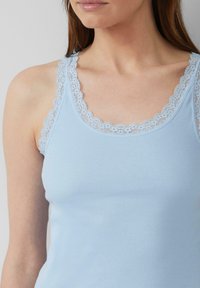 Lichtblauw geribbeld tanktop met delicate kantafwerking langs de halslijn en bandjes, dat de zachte textuur en de aansluitende pasvorm benadrukt.