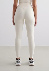 Leggings crema realizzati in un tessuto morbido e elasticizzato; con vita alta e design aderente. Abbinati a scarpe da ginnastica nere e bianche.