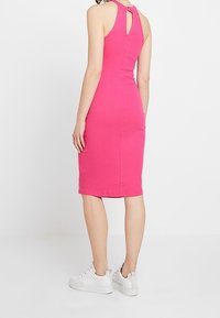 Upnuté midi šaty z jasně růžového žebrovaného materiálu, s výřezem na zádech, bez rukávů a kombinované s bílými teniskami.
