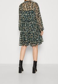 Černé šaty s květinovým vzorem a poloprůhledným materiálem, dlouhé rukávy, nařasený pas a sukni s volány. Doplněné černými kotníkovými botami na podpatku.