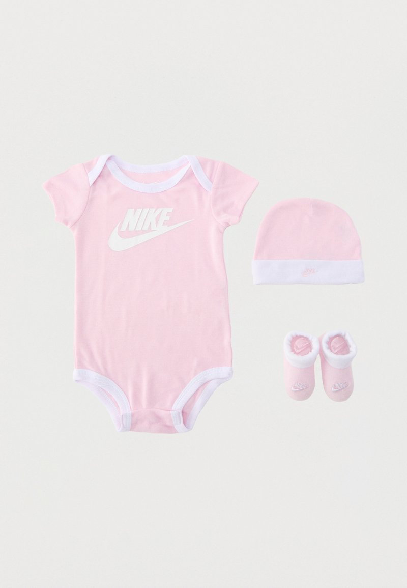 Ensemble bébé Nike rose avec body manches courtes, bonnet assorti et chaussons doux, tous avec des bordures blanches et détails du logo.