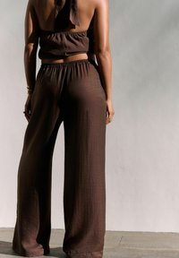 Hnědý, lehký dvoudílný outfit skládající se z krátkého topu se zavazovacím zadním dílem a kalhot s širokými nohavicemi a elastickým pasem. Texturovaná tkanina.