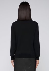 Černý svetr s kulatým výstřihem a dlouhými rukávy, zobrazený zezadu, s žebrovaným lemem a manžetami, nošený na kožené sukni.