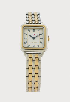Montre-bracelet carrée argent et or avec cadran blanc, chiffres romains, bracelet métal bicolore et logo Tommy Hilfiger à 12 heures.