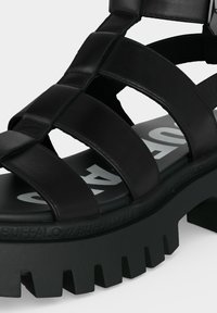 Μαύρο chunky πέδιλο πλατφόρμα με χοντρές διασταυρούμενες λουριά και ανθεκτική σόλα με έντονο λευκό κείμενο στο πέλμα.