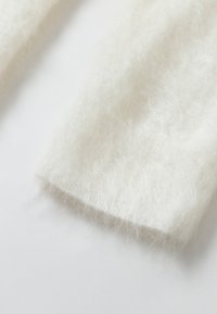 Tessuto lavorato a maglia bianco e soffice con una superficie morbida e testurizzata. I bordi sono leggermente arrotondati, mettendo in evidenza un aspetto accogliente.