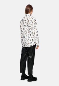 White long-sleeve shirt with colorful dog illustrations, paired with black shiny trousers. The shirt has a button-down collar and loose fit.