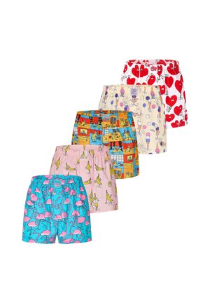 Hemdloser Mann trägt weiße Boxershorts mit rotem Herzmuster mit Cartoon-Augen und Armen, steht vor einem schlichten hellen Hintergrund.