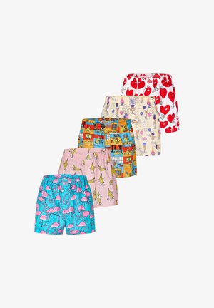 Hemdloser Mann trägt weiße Boxershorts mit rotem Herzmuster mit Cartoon-Augen und Armen, steht vor einem schlichten hellen Hintergrund.
