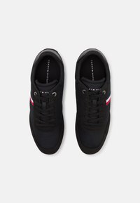 Para czarnych trampek Tommy Hilfiger z sznurówkami, z czerwonymi i białymi paskami po bokach, widoczna z góry na białym tle.