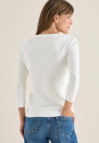 Witte, aangesloten top met driekwart mouwen, ronde halslijn, gladde textuur, gecombineerd met blauwe spijkerbroeken met achterzakken.