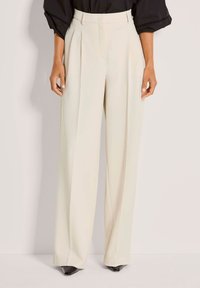 Roomy cremewitte broek met rechte pijpen, gemaakt van gladde stof, met voorplooien en een hoge taille. Gecombineerd met zwarte pumps met een puntige neus.