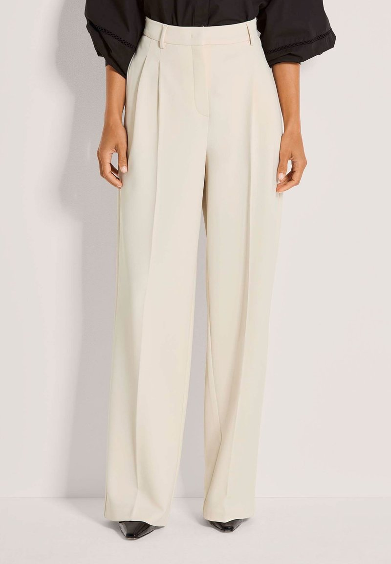 Roomy cremewitte broek met rechte pijpen, gemaakt van gladde stof, met voorplooien en een hoge taille. Gecombineerd met zwarte pumps met een puntige neus.