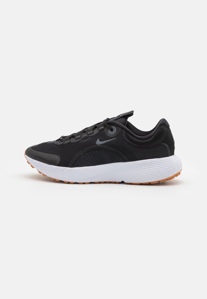 Zapatilla deportiva negra con parte superior de malla, suela de goma, un branding sutil y una entresuela blanca con detalles texturizados y suela de goma.