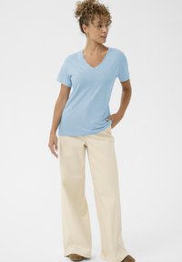 Hellblaues T-Shirt mit V-Ausschnitt und kurzen Ärmeln, kombiniert mit beigen Hosen mit weitem Bein. Weicher Stoff und entspannte Passform. Lässiges Design mit minimalen Details.