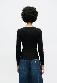 Top preto de manga comprida com design ajustado e decote redondo, combinado com calças largas de ganga azul com bolsos e etiqueta de logótipo.