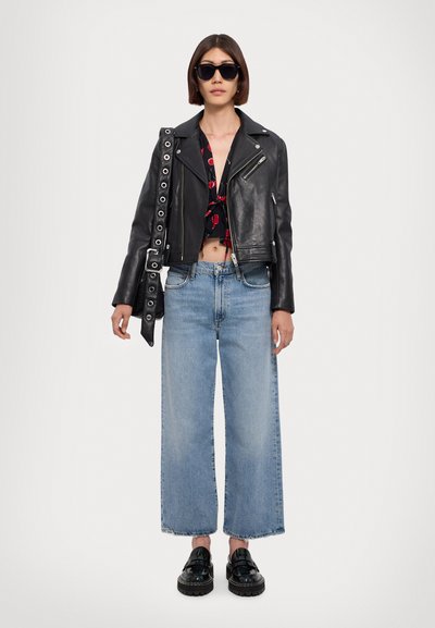 Giacca in pelle nera da biker, design corto, abbinata a un top floreale corto, jeans in denim a gamba larga e scarpe platform nere. Occhiali da sole neri indossati.