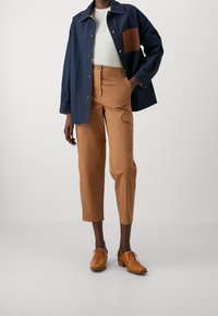 Námořnický modrý kabát s hnědým nášivem, bílý žebrovaný top a světlé cargo kalhoty. Hnědé šněrovací boty s nízkým podpatkem dotvářejí celý outfit.