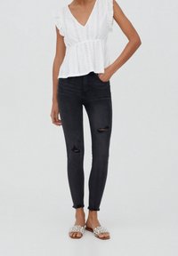 Valkoinen reikäpitsipaita, jossa röyhelöhihat, yhdistetty mustiin kapealahkeisiin farkkuihin, joissa on polvireiät. Jalkineina koristellut liukusandaalit.