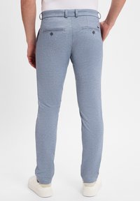 Lichtblauwe geweven broek met een gestructureerde afwerking, slim fit, zij- en achterzakken, en ceintuurlussen. Gecombineerd met witte schoenen.